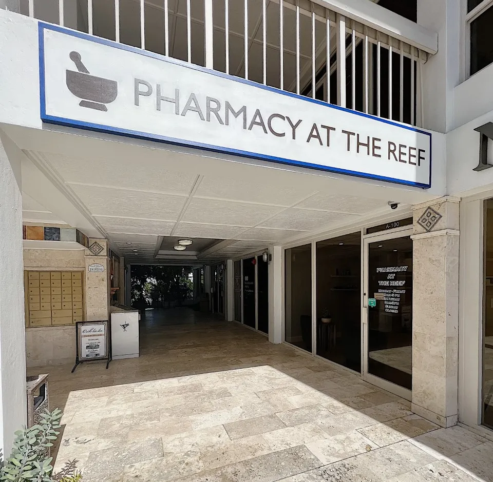 Entrance to "Pharmacy at the Reef" with a sign above and glass doors below.