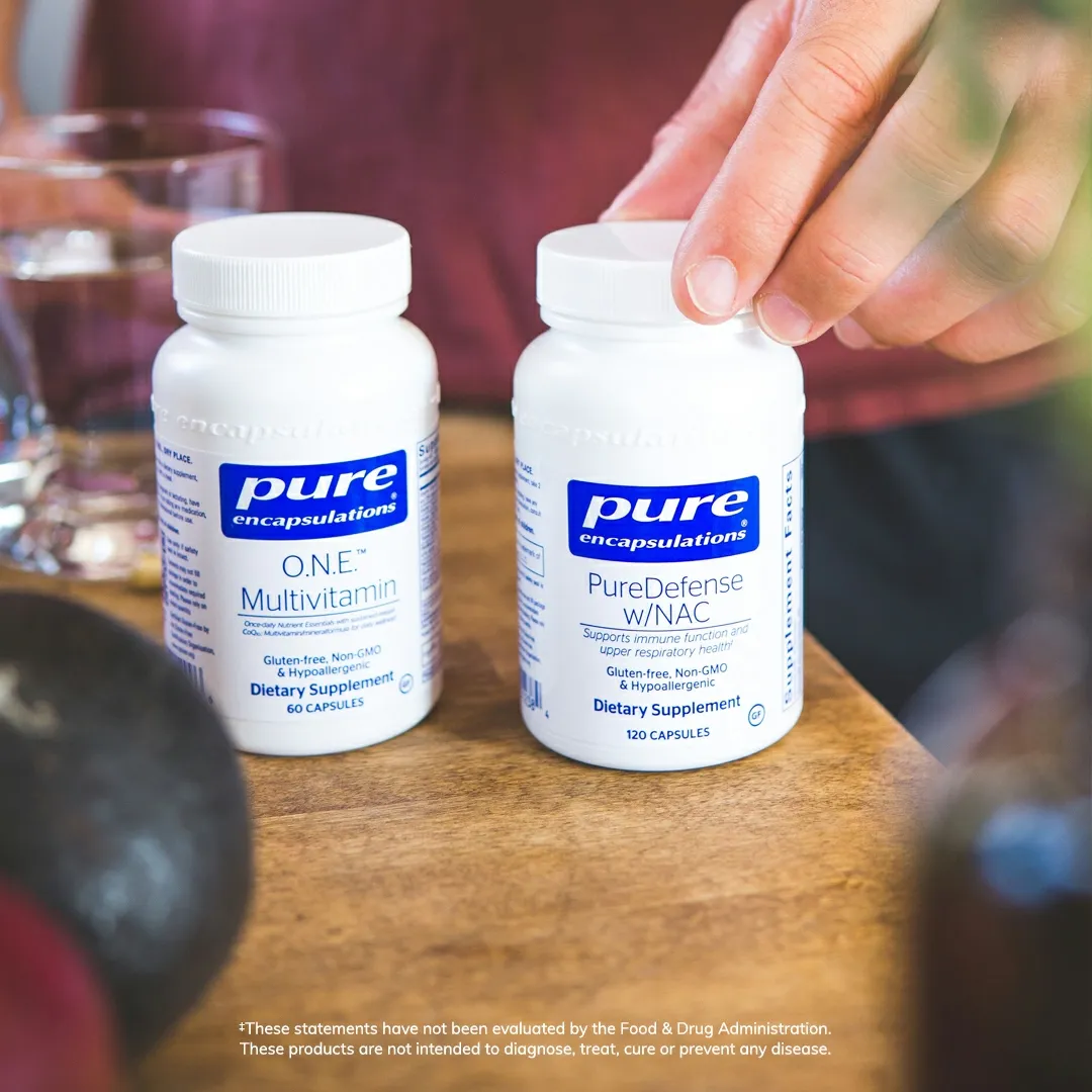 Two bottles of Pure Encapsulations supplements on a table with someone's hand nearby.