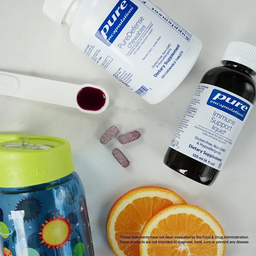 Supplements, a children's cup, orange slices, and a spoon with liquid on a white surface.