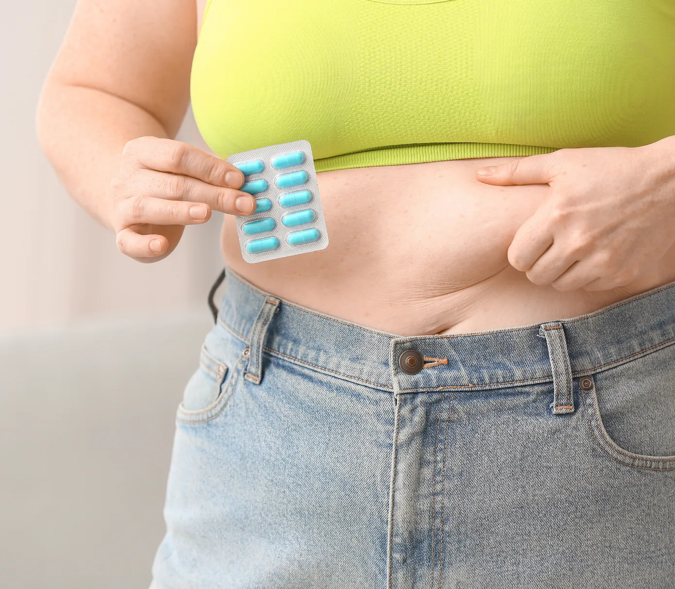 Person in a lime green top holding a blister pack of blue pills near their stomach.