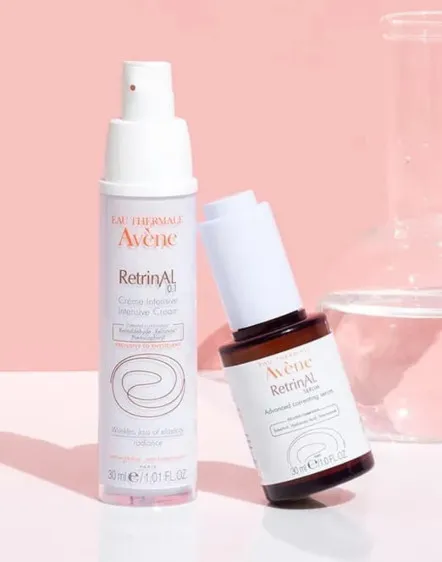 Two Avene RetrinAL skincare products on a pink background with a glass beaker in the background.