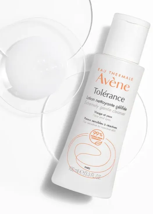 Bottle of Avène Tolérance Extremely Gentle Cleanser on a white surface with clear, round dishes.