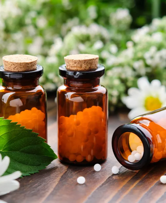 Three brown glass bottles with cork stoppers, filled with small white pills, surrounded by green leaves and flowers.